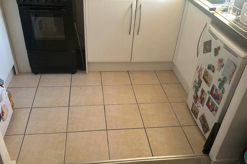 A kitchen floor covered in dated cream ceramic tiles before replacement.