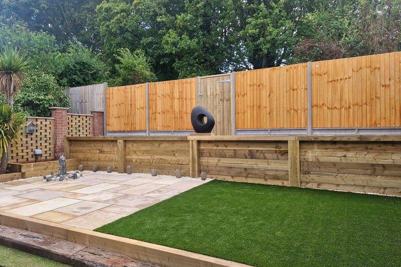 The same garden finished, with new close-board fencing, sleeper retaining beds, sandstone paving and a lawn.
