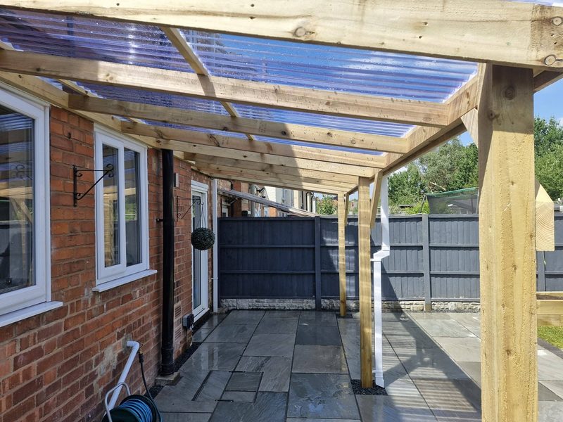 The view along the underside of a timber canopy, showing the rafters and clear roof sheets above a patio.