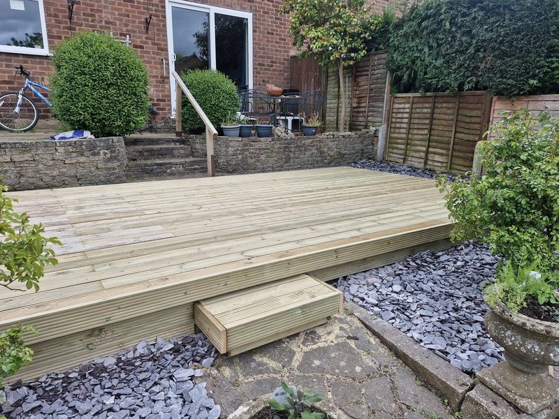 New timber decking with a step down onto slate chippings, laid across a rear garden.