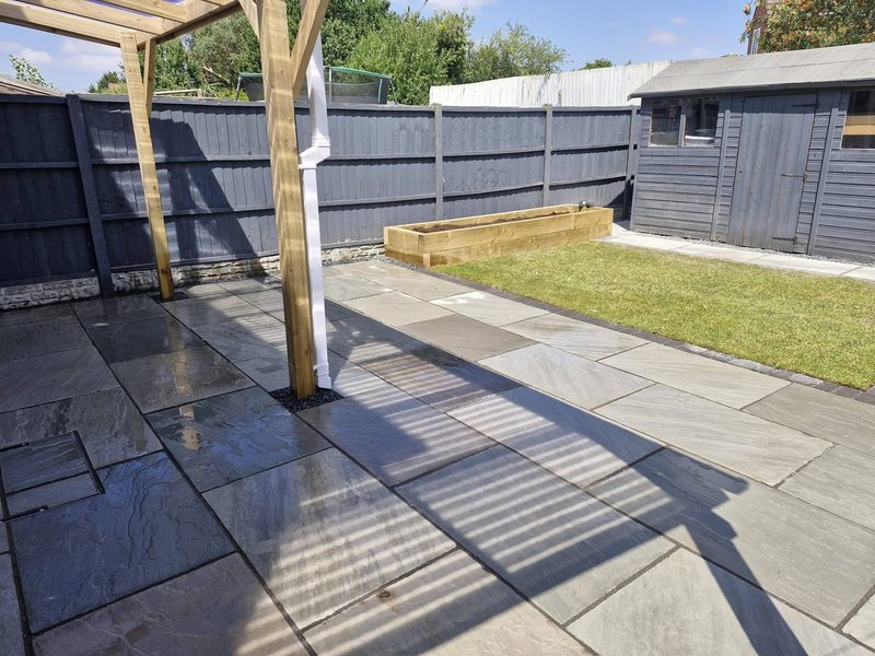 A finished rear garden with grey sandstone patio, timber pergola posts, a raised sleeper bed and new turf.