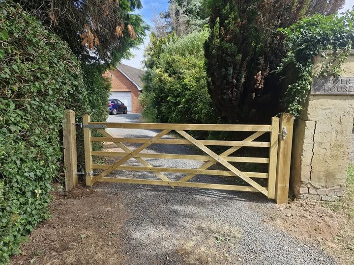 A five-bar timber driveway gate hung between new posts at the entrance to a gravel drive.