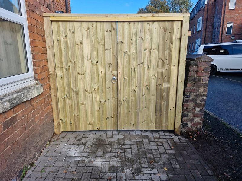 A pair of close-boarded timber driveway gates hung between a house wall and a brick pillar.