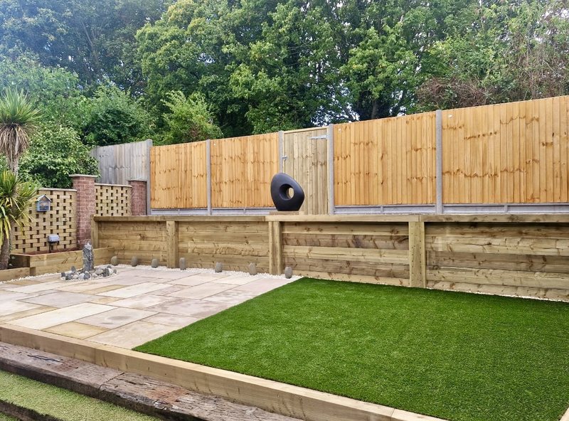 A completed rear garden in Droitwich Spa with new close-board fencing and gate, sleeper retaining beds, sandstone paving and an artificial lawn.